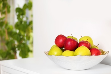 Bowl with different sweet apples on commode in room, space for text