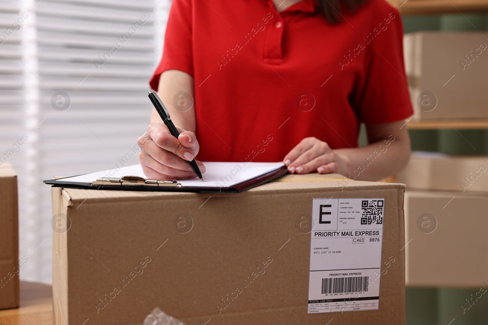 Photo of Parcel packing. Post office worker with clipboard and box indoors, closeup