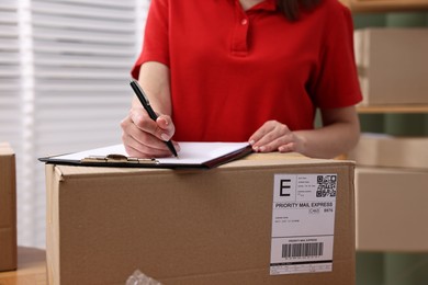 Parcel packing. Post office worker with clipboard and box indoors, closeup