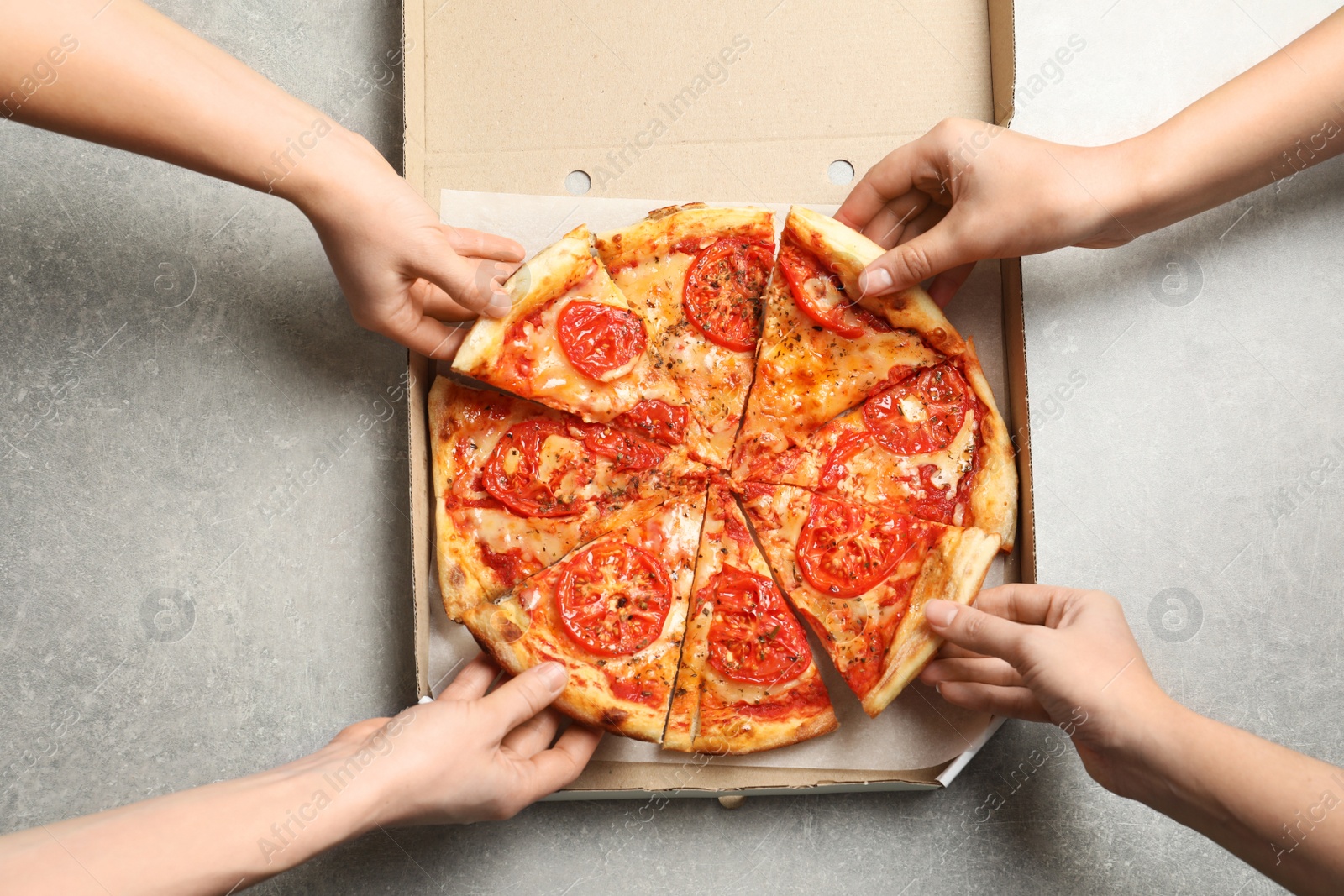 Photo of Young people taking slices of hot cheese pizza from cardboard box at table, top view. Food delivery service