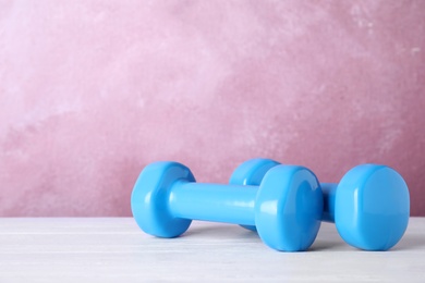 Stylish dumbbells on table against color background, space for text. Home fitness