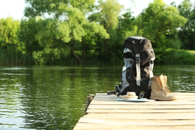 Photo of Backpack and camping equipment on wooden pier near river. Space for text