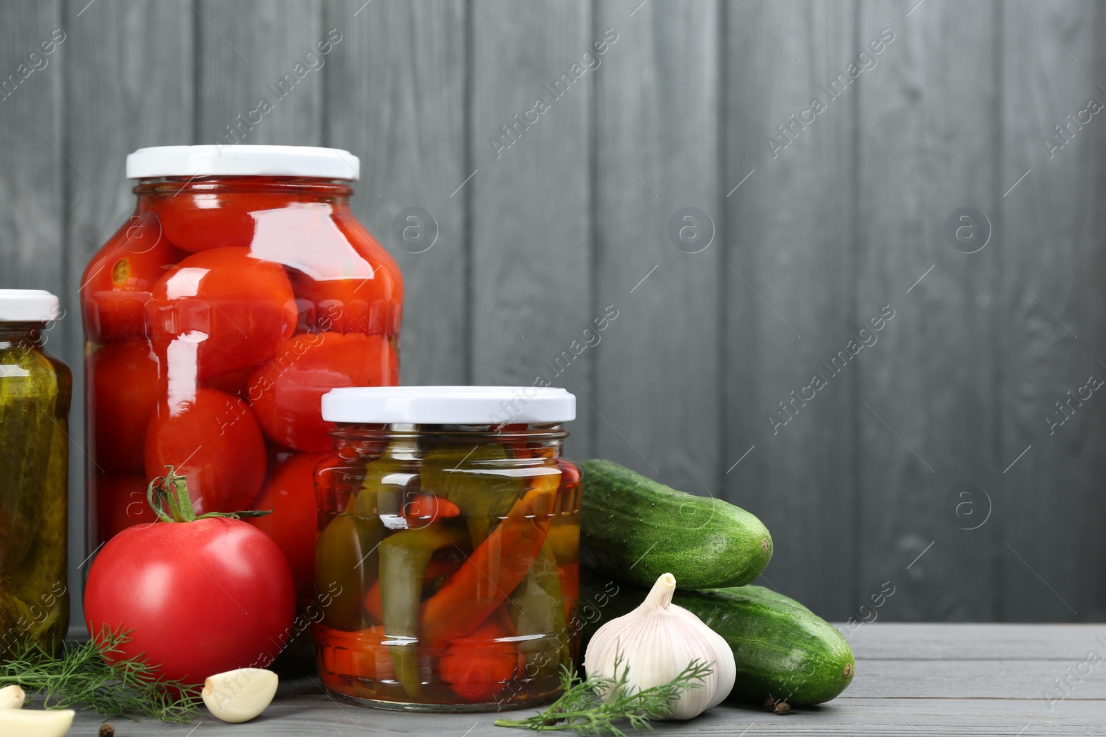 Photo of Glass jars with different pickled vegetables on grey wooden background. Space for text