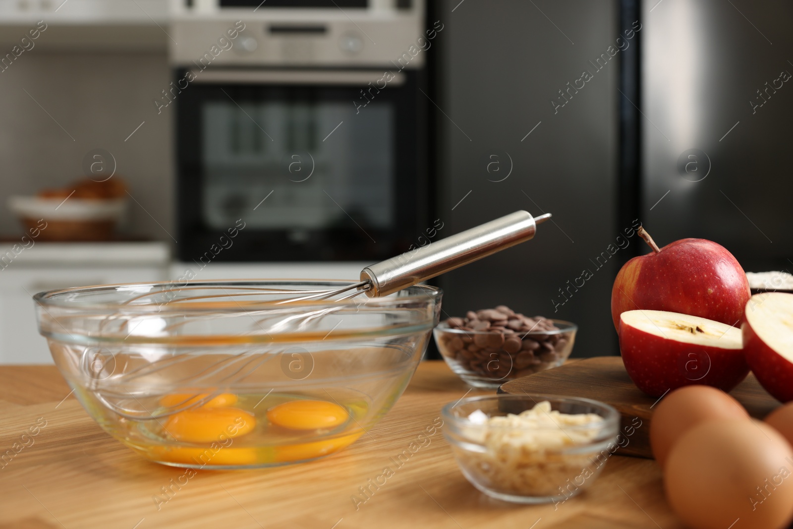 Photo of Cooking process. Metal whisk, bowl and products on wooden table in kitchen, closeup