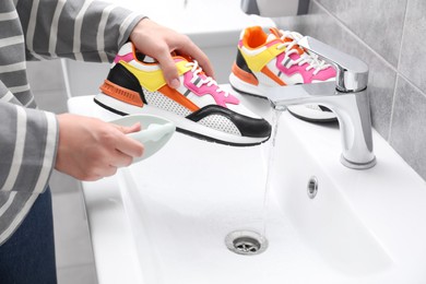 Photo of Woman washing stylish sneakers with brush in sink, closeup