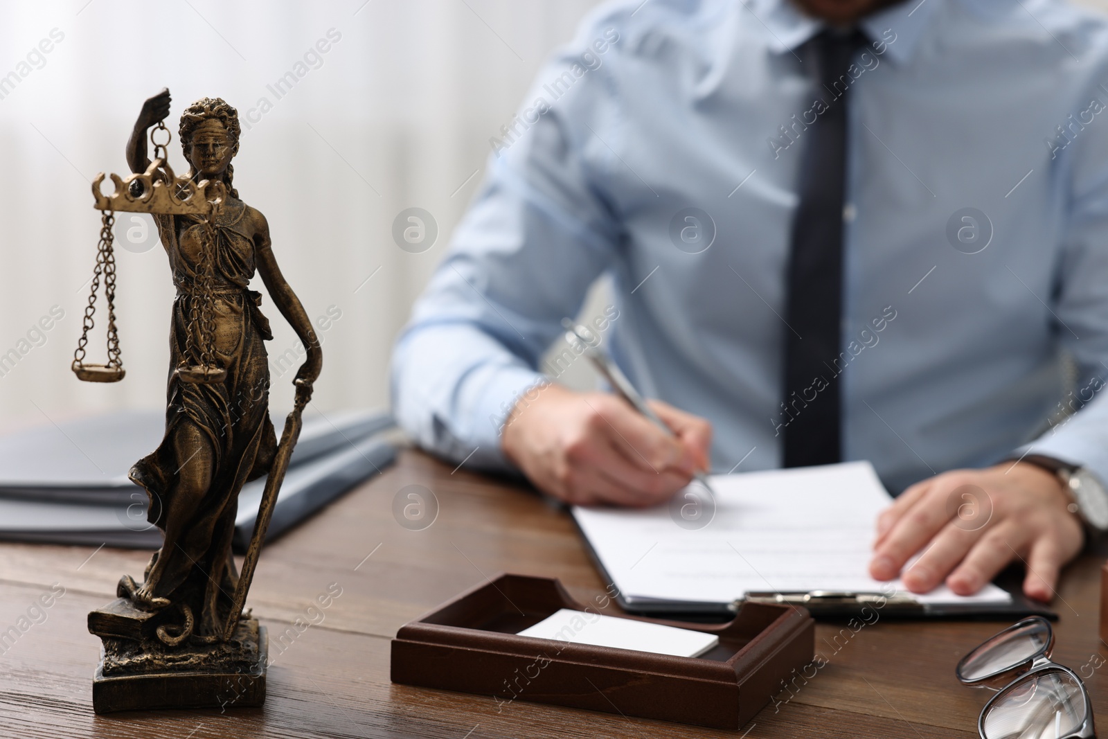 Photo of Lawyer working at wooden table in office, focus on statue of Lady Justice