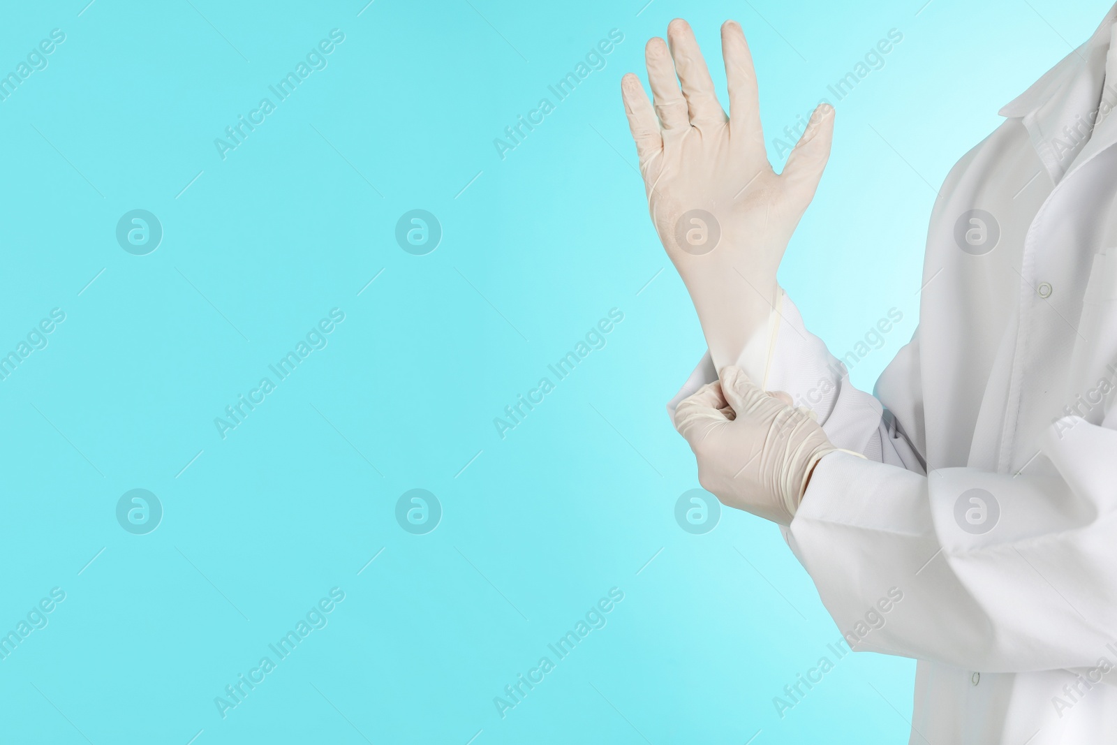 Photo of Male doctor putting on rubber gloves against color background, closeup with space for text. Medical object