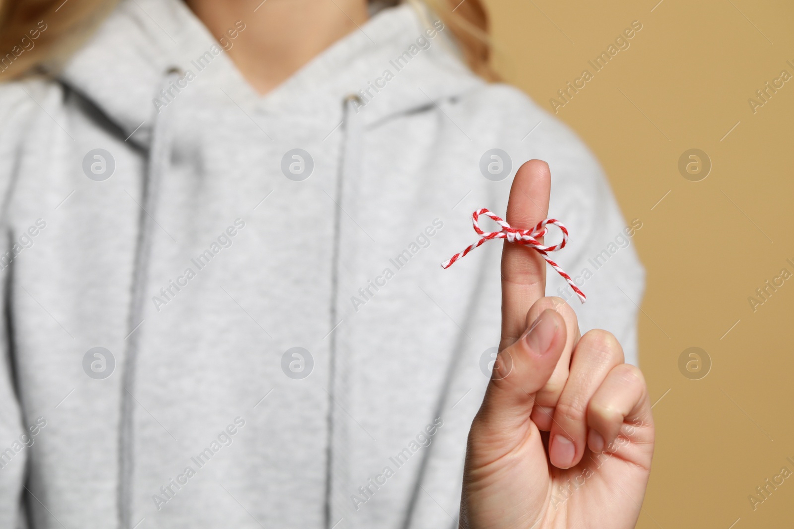 Photo of Woman showing index finger with tied bow as reminder against light brown background, focus on hand