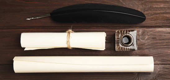 Quill, inkwell and paper rolls on wooden table, flat lay. Banner design