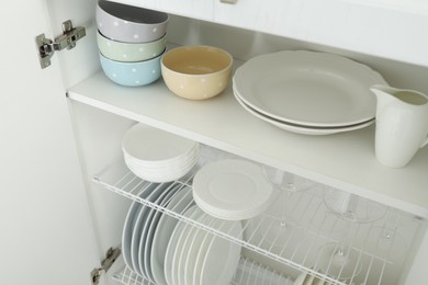 Clean plates, bowls and glasses on shelves in cabinet indoors