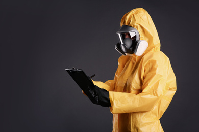 Woman in chemical protective suit holding clipboard on grey background, space for text. Virus research
