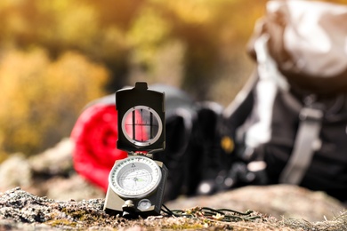 Photo of Compass on rock against blurred background, space for text. Camping equipment