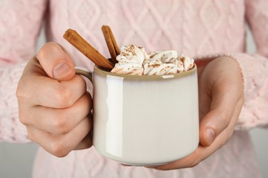 Photo of Woman holding cup of delicious hot chocolate with marshmallows and cinnamon sticks, closeup