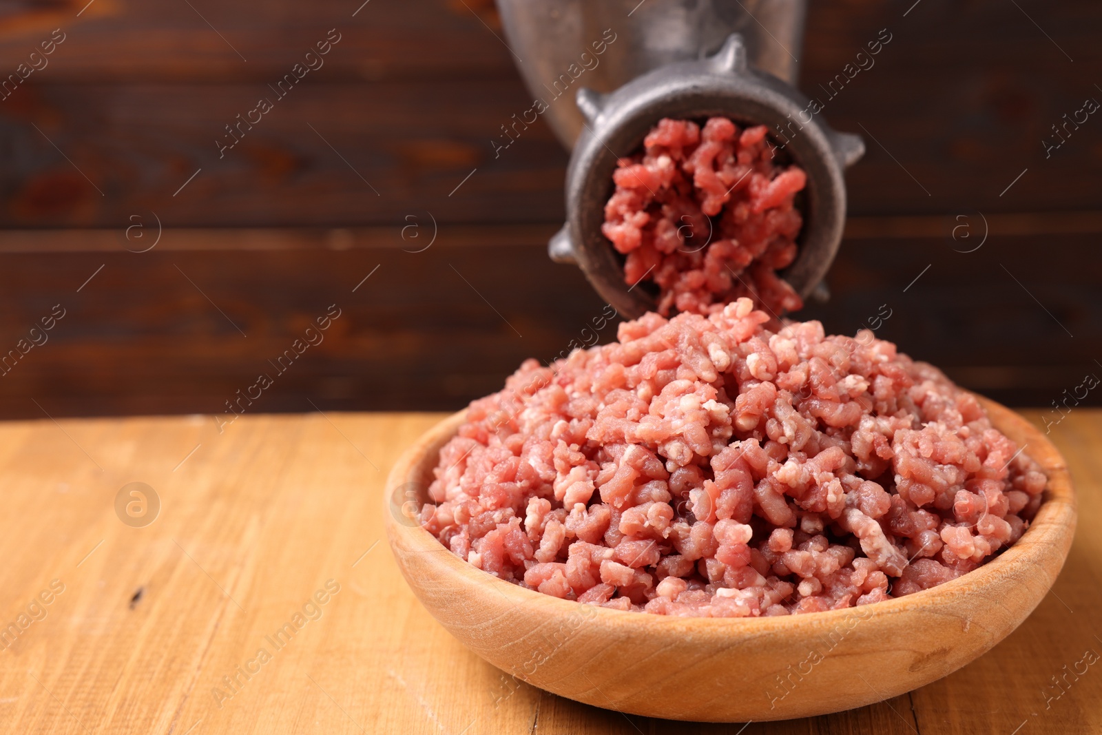 Photo of Manual meat grinder with beef mince on wooden table, closeup. Space for text