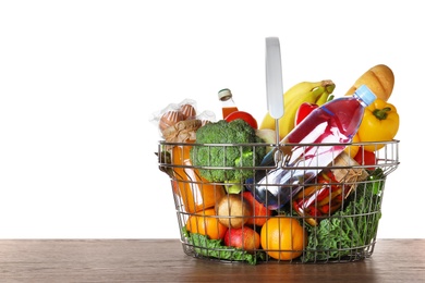 Photo of Shopping basket with grocery products on wooden table against white background. Space for text