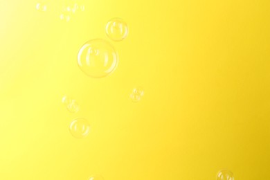 Photo of Beautiful transparent soap bubbles on yellow background