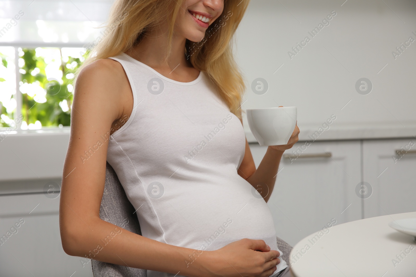 Photo of Beautiful pregnant woman drinking tea in kitchen, closeup