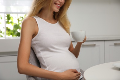 Photo of Beautiful pregnant woman drinking tea in kitchen, closeup