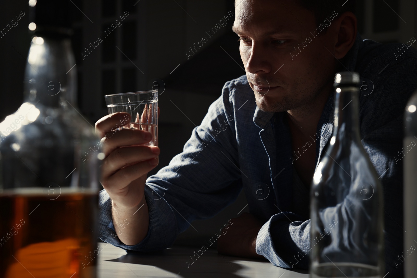 Photo of Addicted man with alcoholic drink at table in kitchen