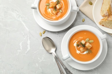 Photo of Tasty creamy pumpkin soup with croutons, seeds and dill in bowls on light grey table, flat lay. Space for text