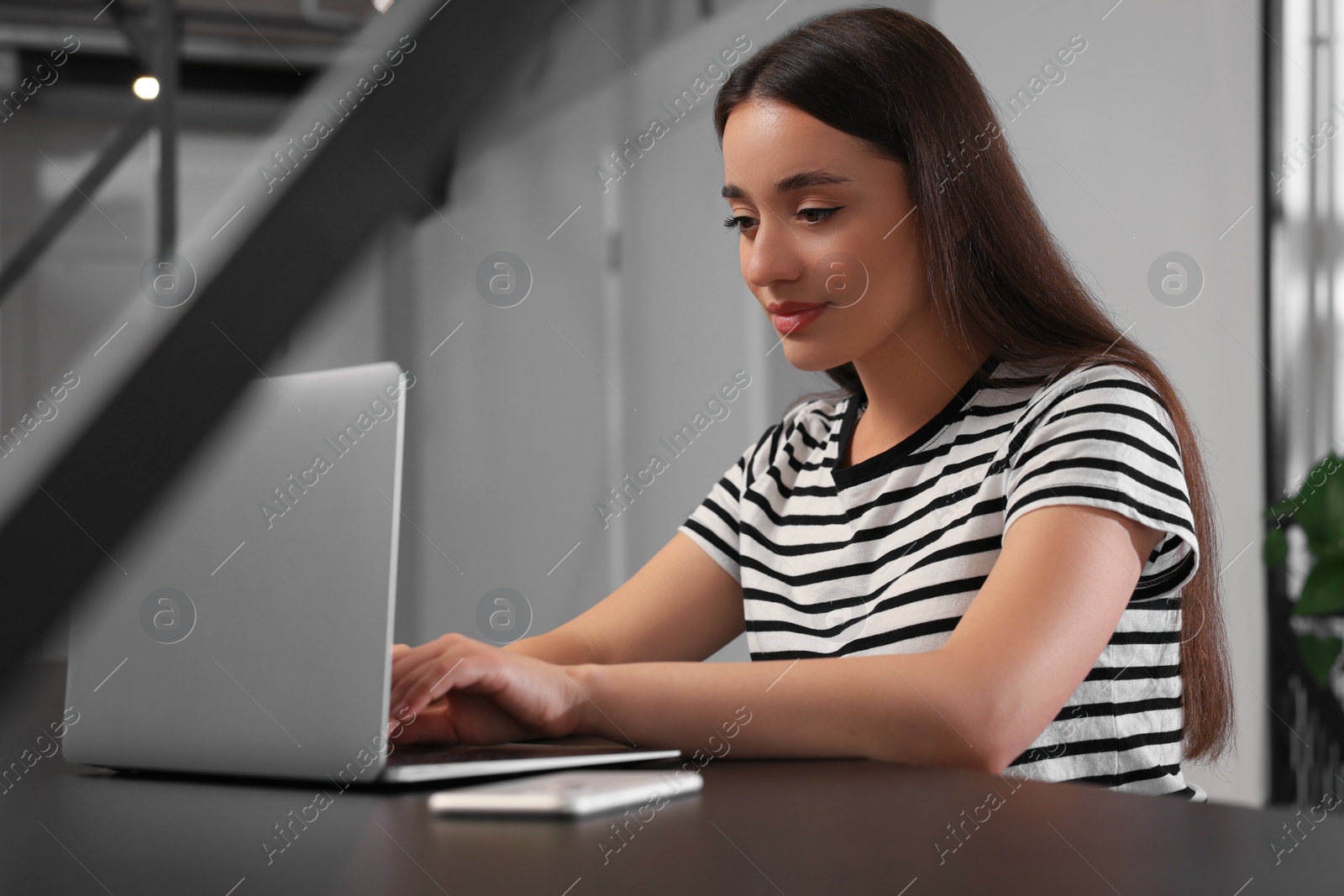 Photo of Young woman using laptop at table in hostel