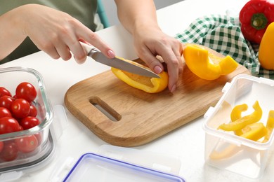 Photo of Woman cutting bell pepper and containers with fresh products on white table, closeup. Food storage