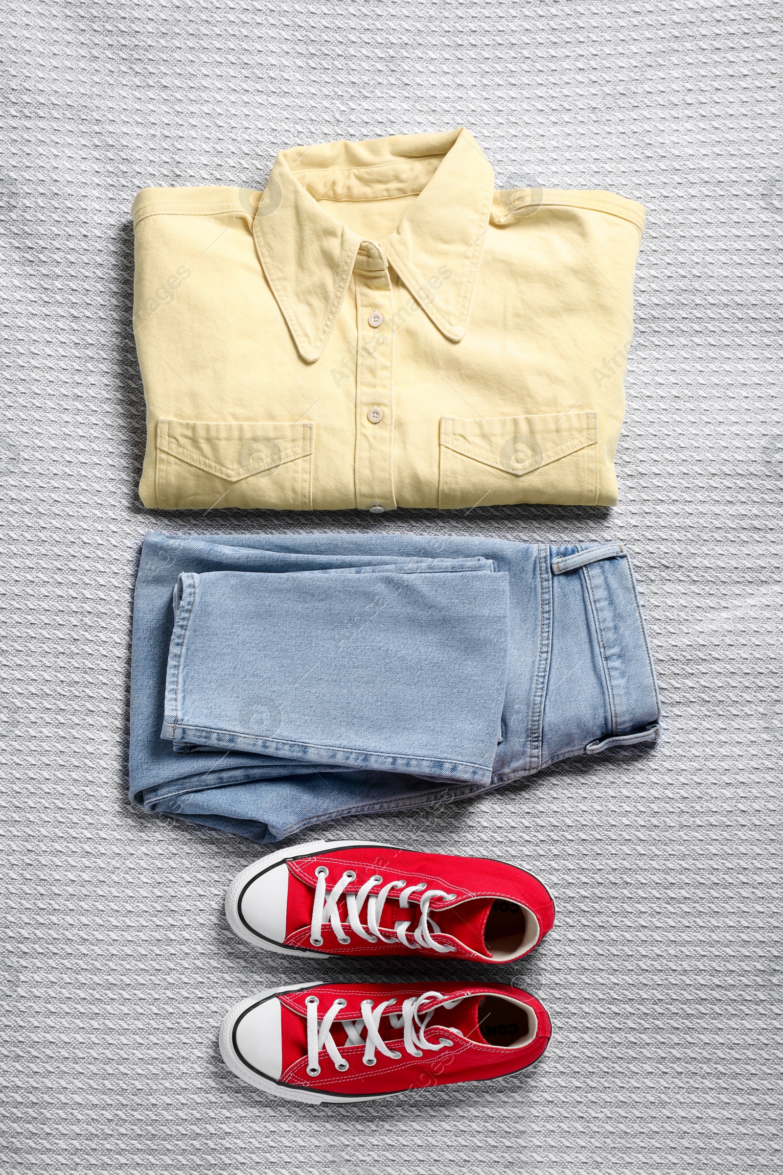 Photo of Pair of stylish red sneakers and clothes on light grey fabric, flat lay