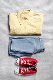 Pair of stylish red sneakers and clothes on light grey fabric, flat lay