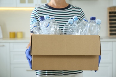 Photo of Woman holding cardboard box with used plastic bottles indoors, closeup. Recycling problem