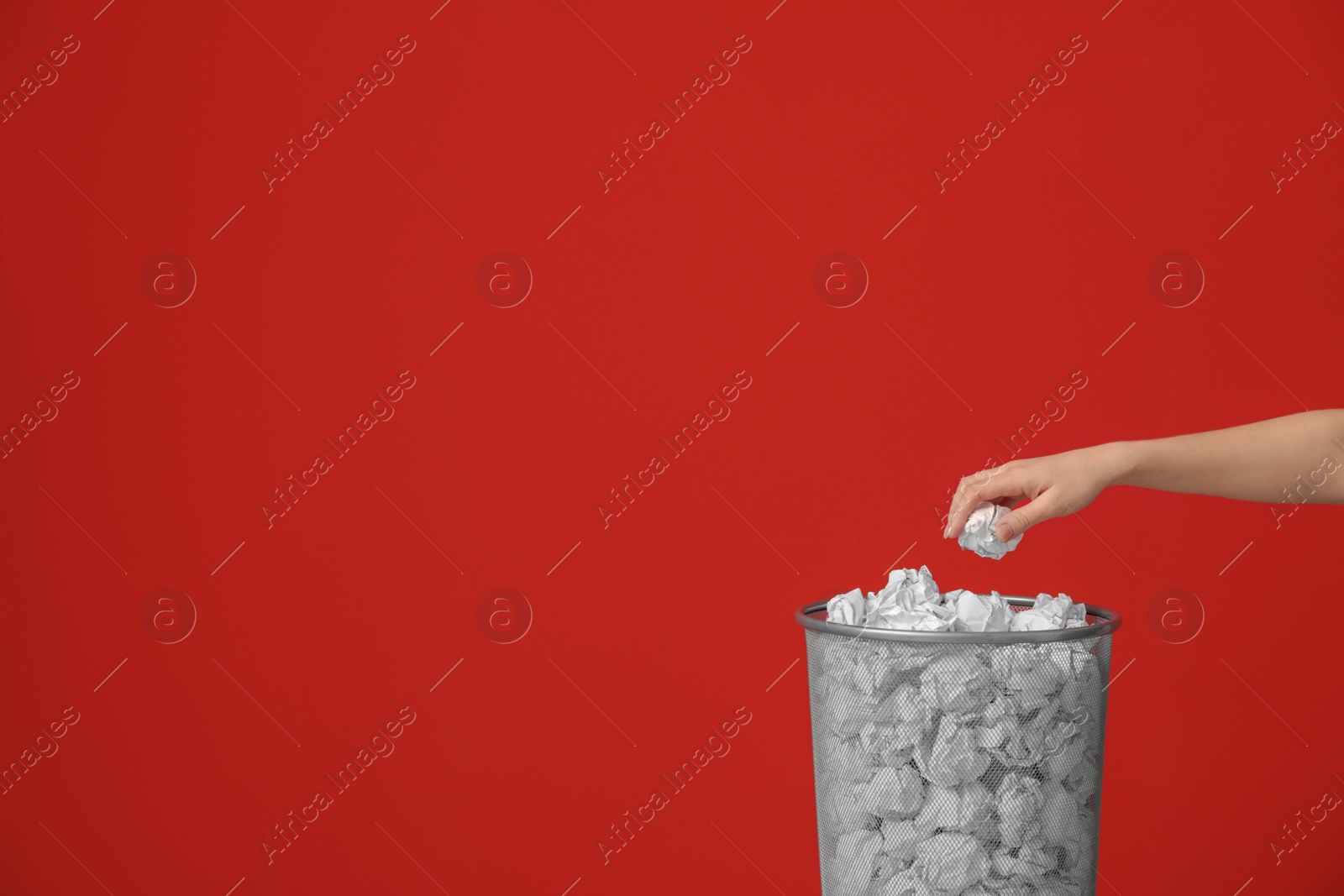 Photo of Woman throwing crumpled paper into metal bin against color background. Space for text