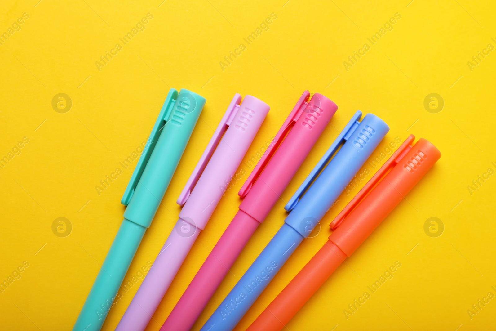 Photo of Many colorful markers on yellow background, above view