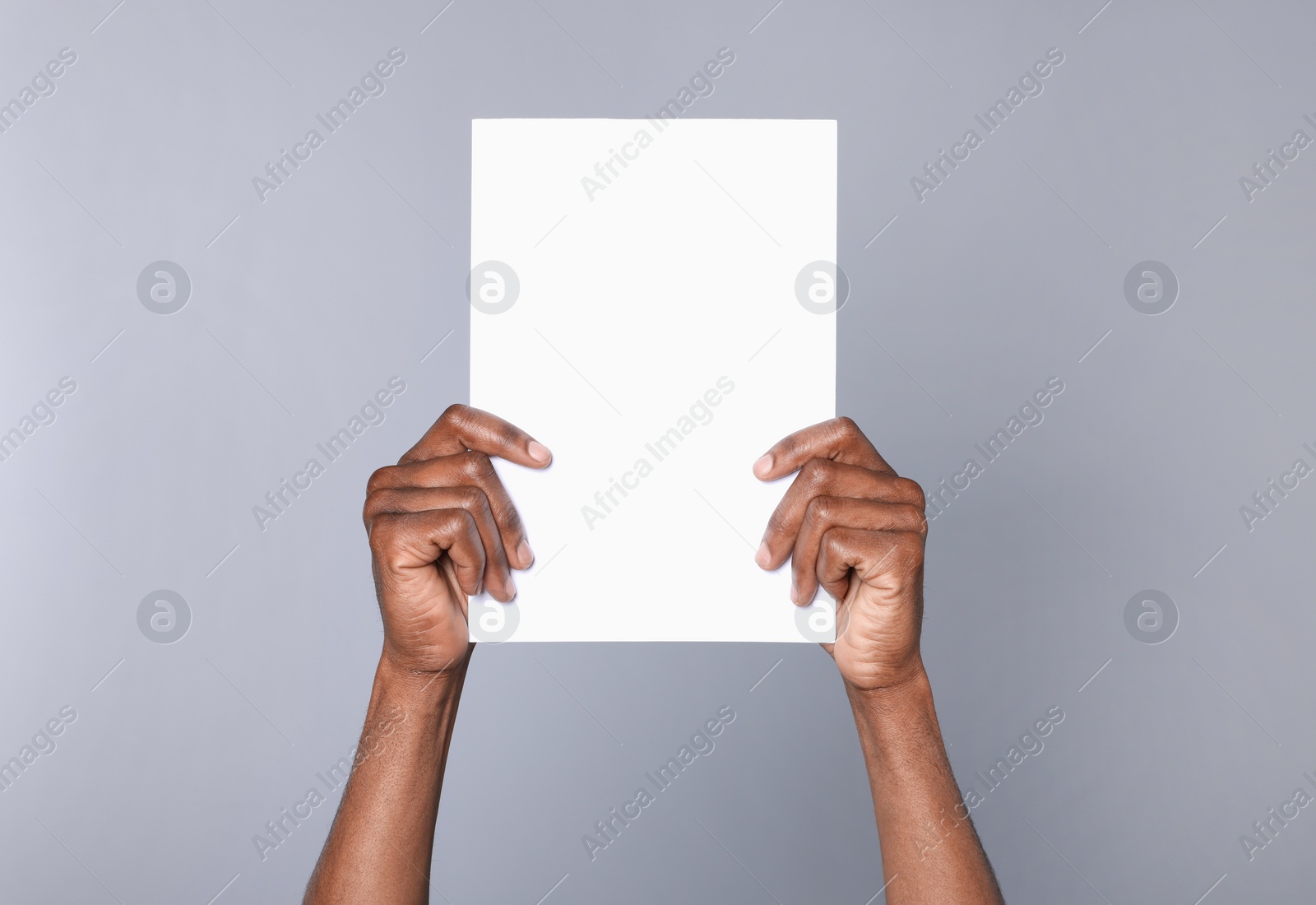 Photo of African American man holding sheet of paper on grey background, closeup. Mockup for design