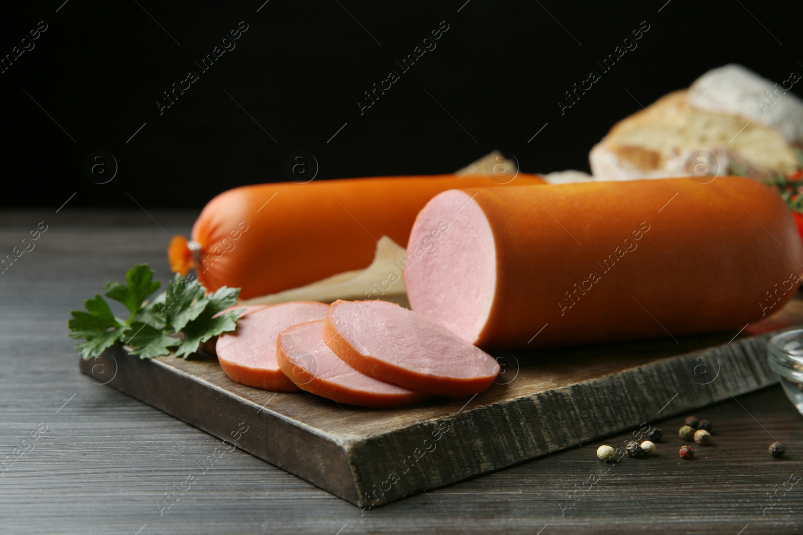 Photo of Board with tasty boiled sausages on dark wooden table against black background, closeup