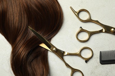 Photo of Professional hairdresser scissors and comb with brown hair strand on grey table, flat lay