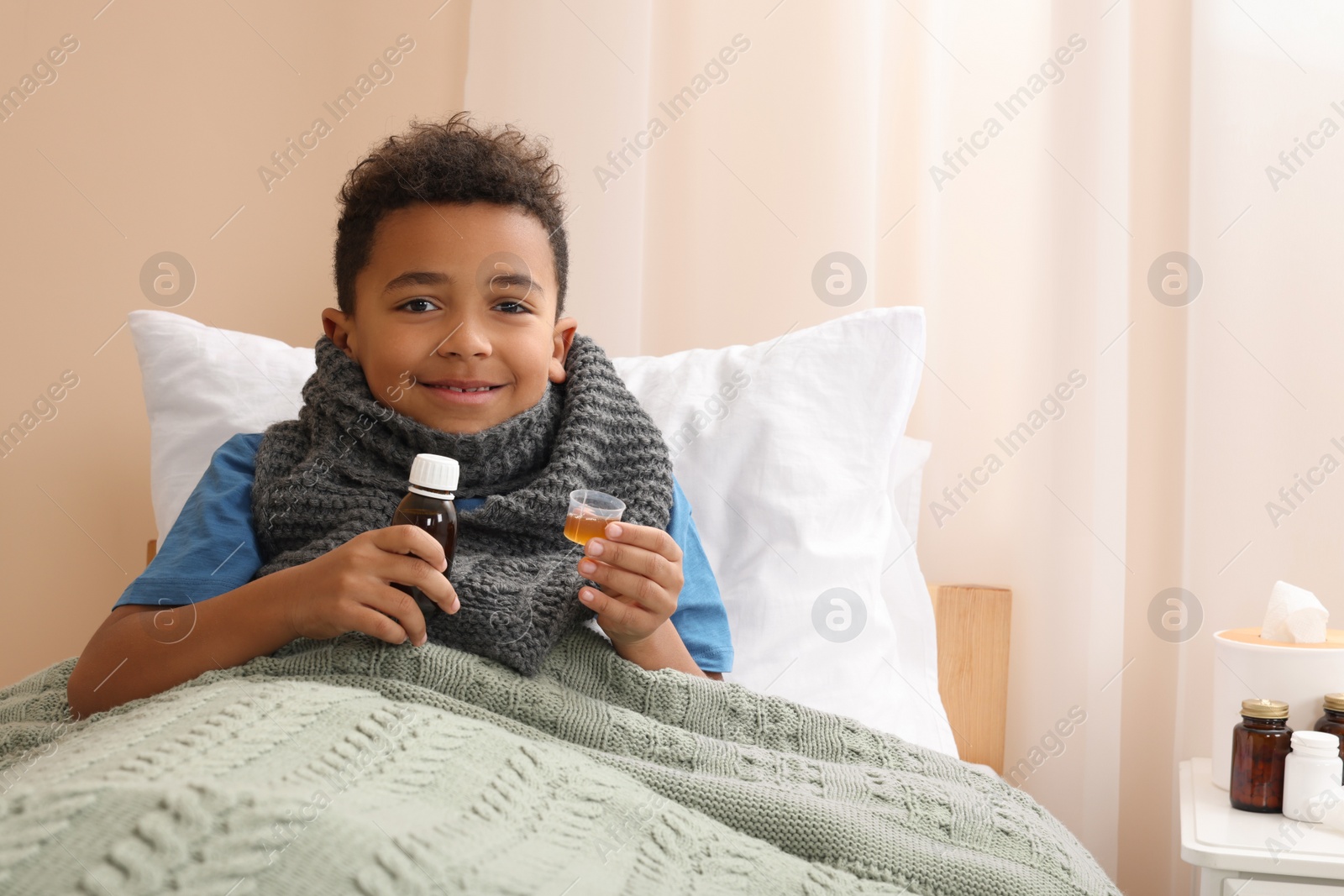 Photo of African-American boy taking cough syrup on bed at home, space for text. Cold medicine