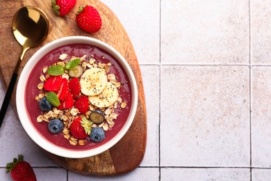 Photo of Delicious smoothie bowl with fresh berries, banana and granola on tiled surface, flat lay. Space for text