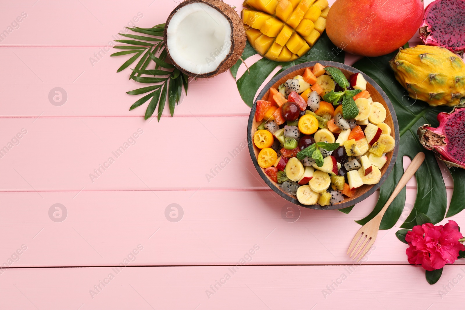 Photo of Flat lay composition with delicious exotic fruit salad on pink wooden table. Space for text