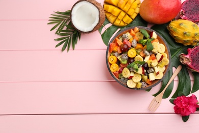 Photo of Flat lay composition with delicious exotic fruit salad on pink wooden table. Space for text