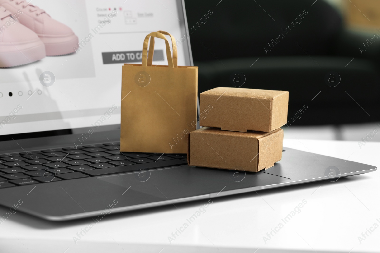 Photo of Online store. Laptop, small shopping bag and mini parcels on white table, closeup