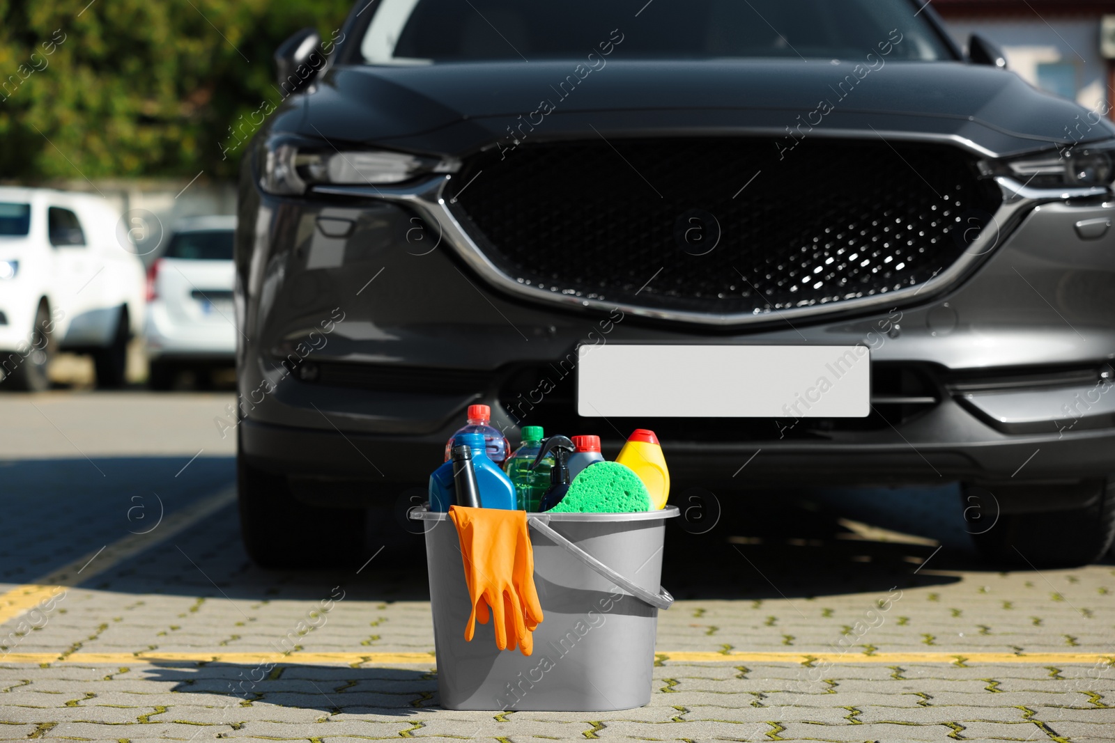 Photo of Car cleaning products in bucket near automobile outdoors on sunny day