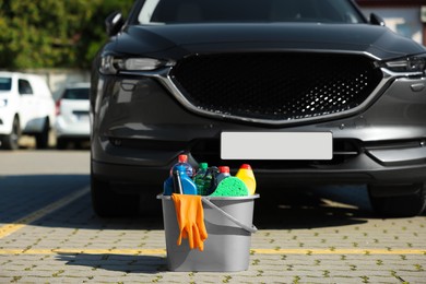 Car cleaning products in bucket near automobile outdoors on sunny day