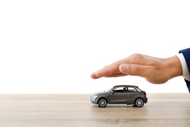 Photo of Insurance agent holding hand over toy car on table against white background, closeup