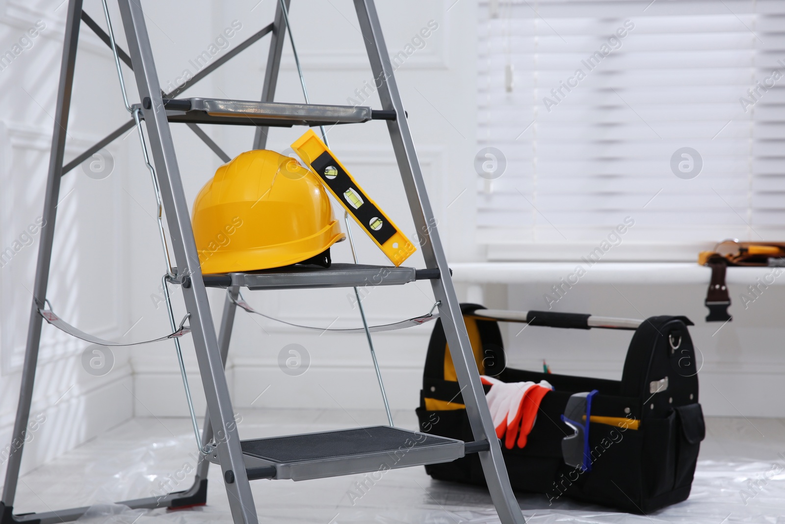 Photo of Metal stepladder with hardhat, level and toolkit indoors