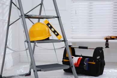 Metal stepladder with hardhat, level and toolkit indoors