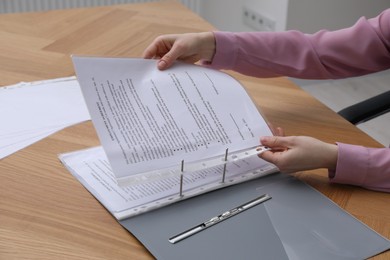 Photo of Woman putting punched pocket with document into folder at wooden table, closeup