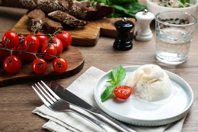 Photo of Delicious burrata cheese with basil and cut tomato served on wooden table