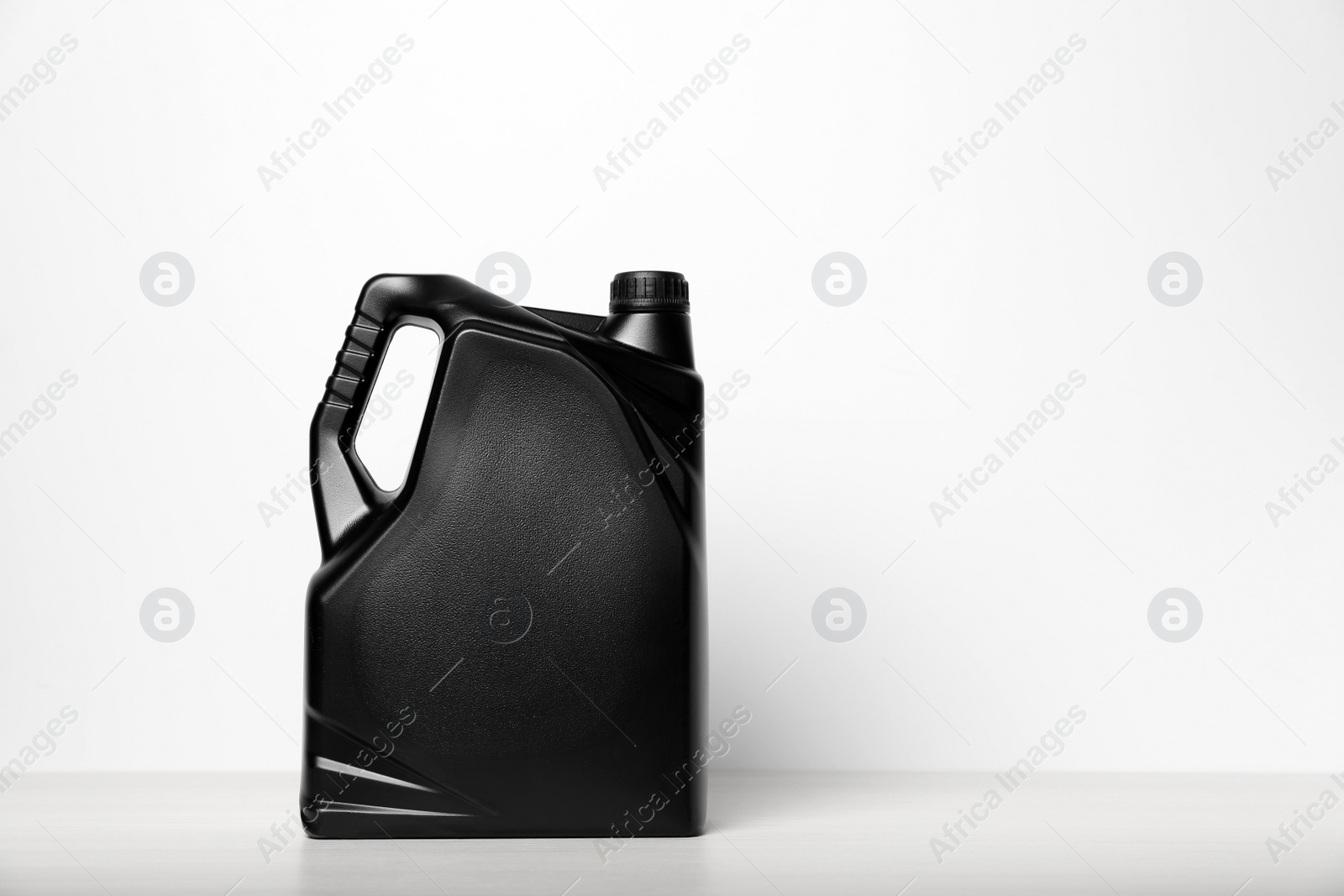 Photo of Motor oil in black canister on table against white background, space for text