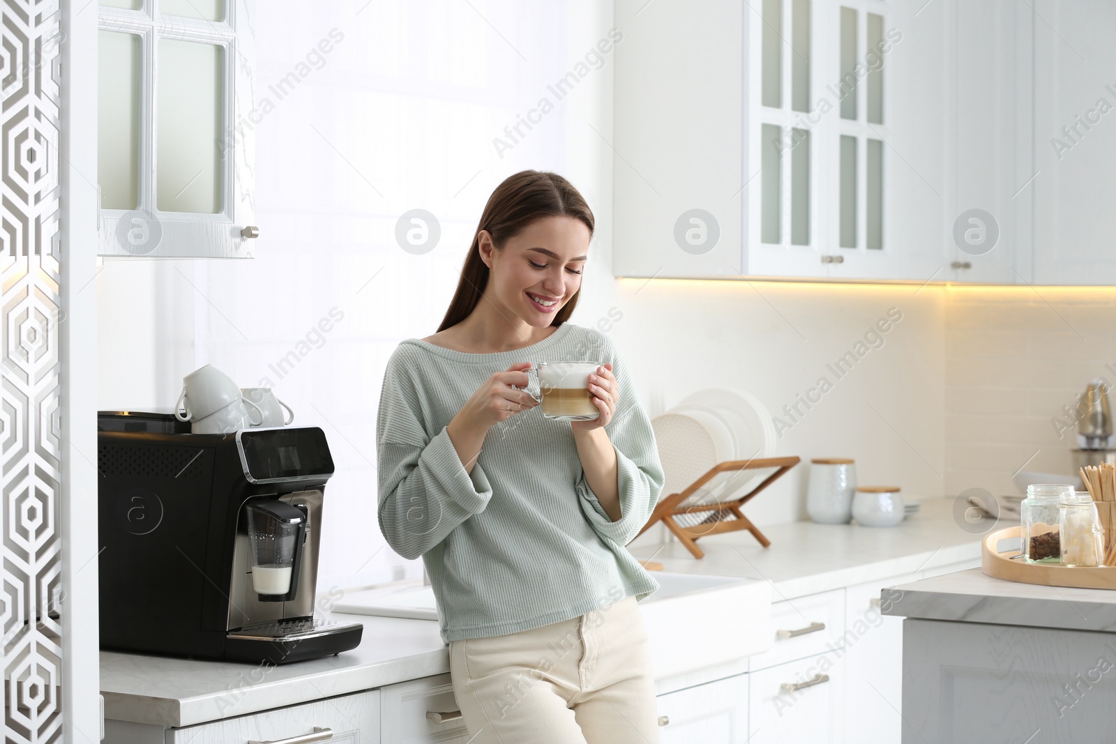 Photo of Young woman enjoying fresh aromatic coffee near modern machine in kitchen