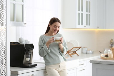 Young woman enjoying fresh aromatic coffee near modern machine in kitchen