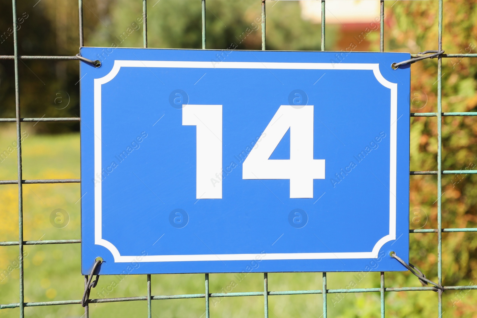 Photo of Plate with house number fourteen hanging on iron fence outdoors, closeup